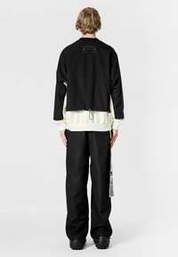 Chaqueta corta negra con forro crema, dobladillo ajustable y detalle de bolsillo en la parte trasera. Combinada con pantalones negros texturizados y zapatos gruesos.