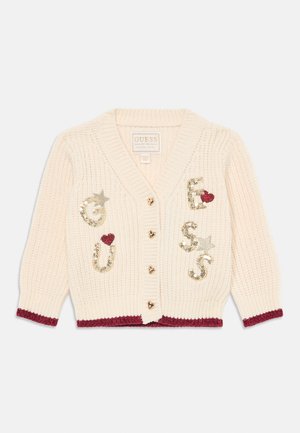 Cardigan en tricot crème avec des boutons dorés en forme de cœur, des bordures bordeaux et des embellissements en sequins écrivant "GUESS" avec des étoiles et des cœurs.