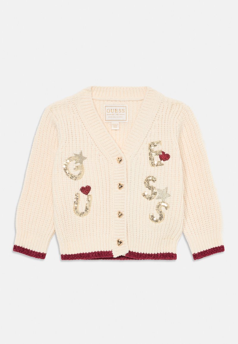 Kremasti pleteni kardigan s zlatnim dugmadima u obliku srca, bordo obrubom i ukrasima od šljokica koji čine natpis "GUESS" s zvijezdama i srcima.