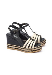 Sandalias de cuña en negro y beige con suela de yute trenzado, que presentan múltiples correas, un diseño de correas en T y un cierre de hebilla en el tobillo.