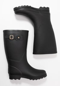 Une paire de bottes de pluie noires en caoutchouc avec des semelles profilées et des boucles décoratives sur les côtés sur un fond blanc.