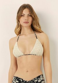 Top de bikini de crochet crema con copas triangulares, lazos a rayas negras y un detalle de encaje intrincado. Combinado con una parte inferior de diseño floral.