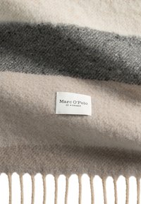 Wełniany koc w beżowo-szare paski z frędzlami na krawędziach oraz białą metką z napisem "Marc O'Polo" i "EST. IN STOCKHOLM."