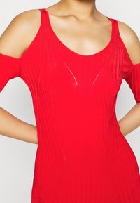 Robe rouge côtelée avec un design épaule dénudée. Confectionnée en matériau extensible, avec des lignes texturées et une silhouette ajustée.
