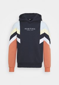 Färgbloxad hoodie i marinblått med blå, gul, svart och orangea detaljer; logotyp framtill tryckt i vitt. Mjuk, texturerad tyg.