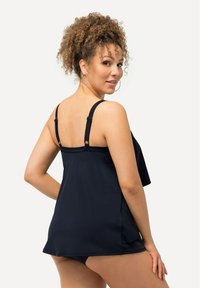 Svart tankini-topp med justerbara band, lätt flödande design och slät textur. Accentuerad med en blygsam botten som kompletterar toppen.