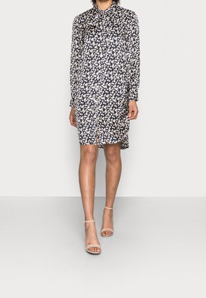 Vestido con estampado floral en azul marino, de manga larga, con botones en la parte delantera, cuello y una abertura. Combinado con sandalias de tiras en tono nude.