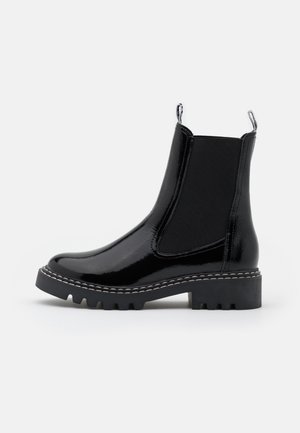 Bota Chelsea negra y brillante con paneles laterales elásticos, suela gruesa con tacos, costuras blancas y tiradores sobre fondo blanco.