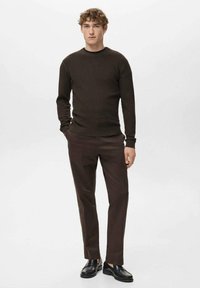 Brauner, gerippter Pullover mit rundem Ausschnitt, kombiniert mit dunkelbraunen Hosen und schwarzen Schuhen, was einen monochromen Look erzeugt.