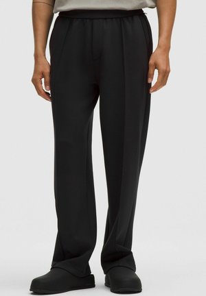 Schwarze, hoch taillierte Hose mit glatter Textur, weitem Bein Design und dezenten vorderen Falten. Kombiniert mit schwarzen Slippern.