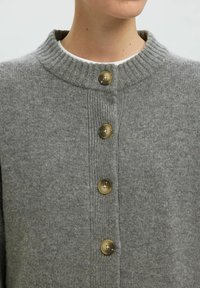 Grau gestrickte Strickjacke mit einem gerippten Kragen, ausgestattet mit fünf runden, hellbraunen Knöpfen und einer weichen Textur.