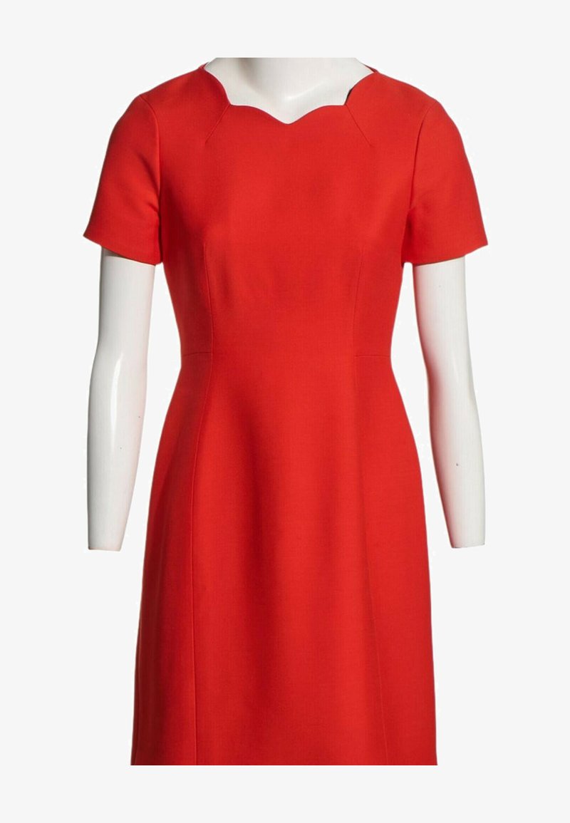Robe rouge à manches courtes avec une taille cintrée et un décolleté original en encoches sur un buste de mannequin blanc.