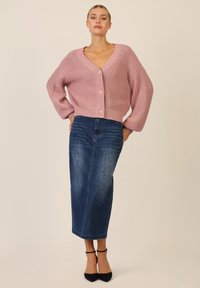 Różowy sweter z dzianiny z dekoltem w kształcie litery V, oversize'owymi rękawami i z przodu zapinany na guziki, w zestawie z dżinsową spódnicą midi z drobnymi ćwiekami i prostym krojem.