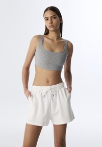 Top corto gris con pequeños adornos plateados y pantalones cortos blancos de cintura elástica con cordón y acentos azules.