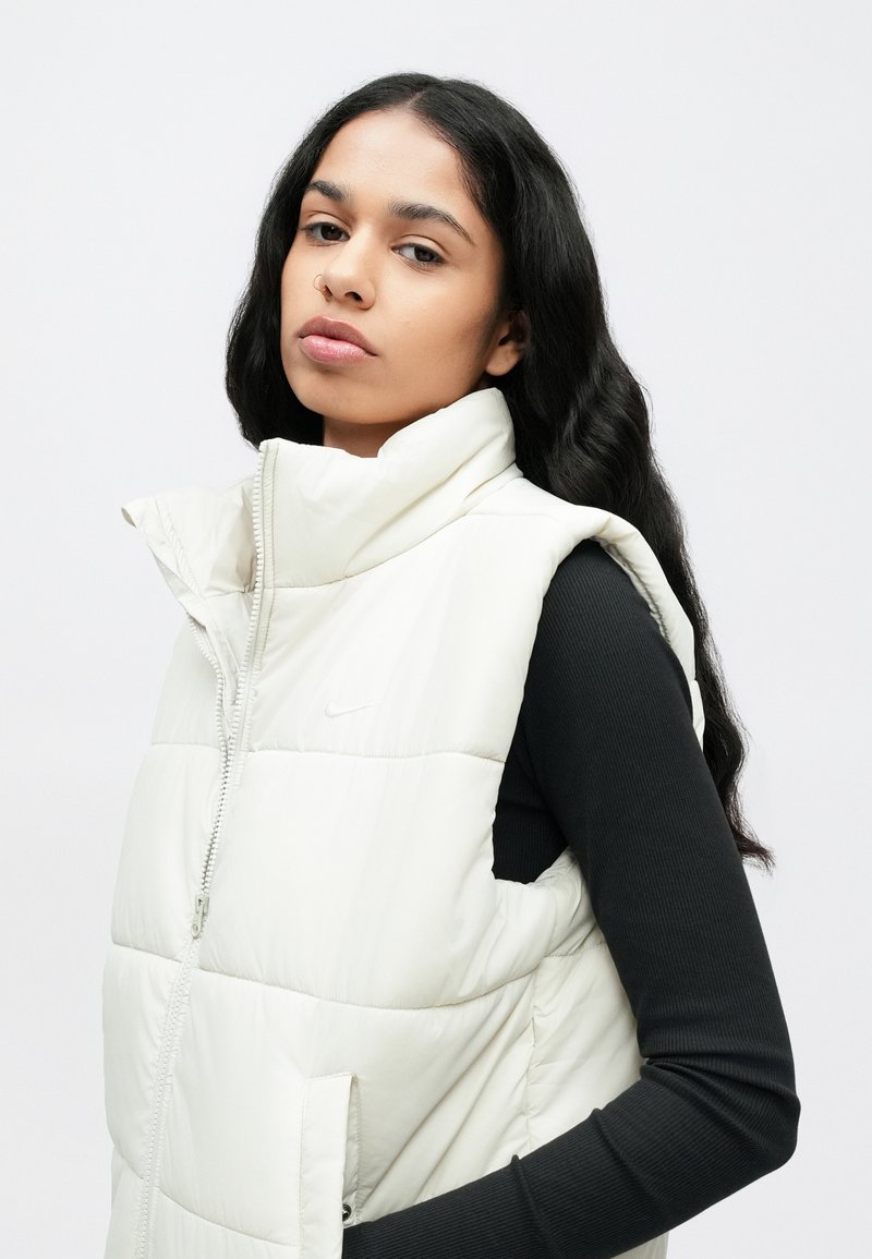 Gepolsterte weiße Weste mit hohem Kragen und Reißverschluss, mit einem dezenten Nike-Logo auf der Brust und strukturierten Nähten für zusätzliche Details.