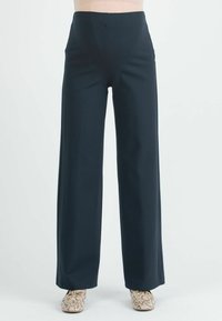 Löysät housut tummansinisenä, valmistettu sileästä kankaasta korkealla vyötäröllä ilman näkyviä taskuja. Tyylitelty yksinkertaisella paidalla ja kuosisilla kengillä.