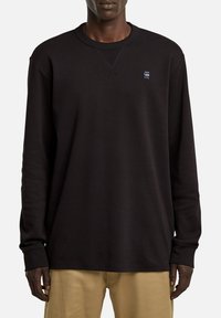 Schwarzer Langarm-Sweatshirt mit Rundhalsausschnitt, gerippten Bündchen und einem kleinen Logo auf der Brust. Glatte Textur und lockere Passform.