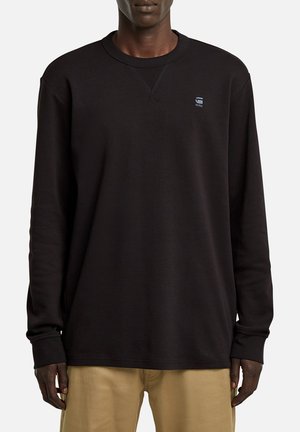 Felpa nera a maniche lunghe con scollatura a girocollo, polsini a costine e un piccolo logo sul petto. Tessuto liscio e vestibilità comoda.