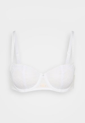 Witte kanten bh met gevoerde cups, verstelbare bandjes en een gouden hardware detail in het midden. Gebogen vorm en gestructureerde stof.
