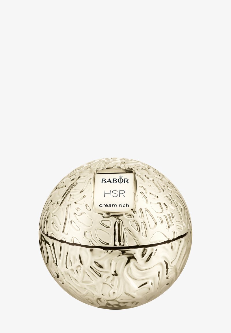 Envase esférico de crema color dorado con patrones de superficie texturizados. La etiqueta muestra "BABOR HSR cream rich" en un rectángulo blanco.