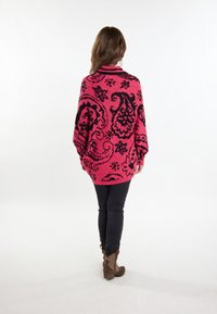 Rosa übergroßer Pullover mit schwarzem Paisleymuster, geripptem Kragen und langen Ärmeln, kombiniert mit schwarzen Hosen und braunen Cowboystiefeln.