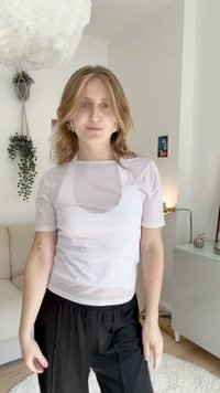 Haut blanc transparent à manches courtes avec un col rond, superposé sur une base plus foncée ajustée. Associé à un pantalon noir ample. Design simple et moderne.