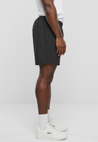 Sorte træningsshorts med elastisk talje, sidelommer og let tekstur. Båret med hvide sneakers og sokker.