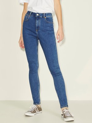 Kõrge vöökohaga sinised skinny teksad, mis on valmistatud denimist. Omab viit taskut, vöökohasippe ja kontrastset õmblust. Kanda hallide tossudega.