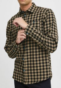 Pánská košile s kostkovaným vzorem v hnědých a černých odstínech, s dlouhými rukávy, modrým zapínáním na knoflíky vpředu a náprsní kapsou.