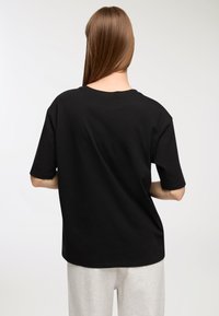 Czarna bawełniana koszulka z krótkim rękawem, okrągłym dekoltem i luźnym krojem. Charakteryzuje się gładką fakturą i jednolitym kolorystyką.