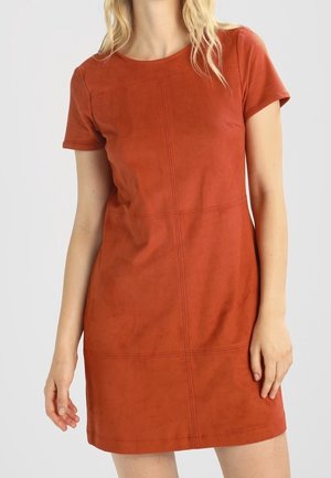 Kvinde iført en kortærmet, rustfarvet kjole i knælængde med synlige sømdetaljer på en ensfarvet baggrund.