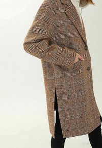 Tarkistettu villakangastakki ruskean sävyissä, jossa on yksirivinen malli, kaksi nappia, sivutaskut ja sivuhalkiot liikkuvuuden helpottamiseksi.