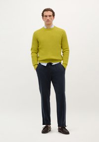 Maglione verde lime con texture, pantaloni navy a vita elasticizzata e scarpe marrone scuro. Collo della camicia visibile sotto il maglione.