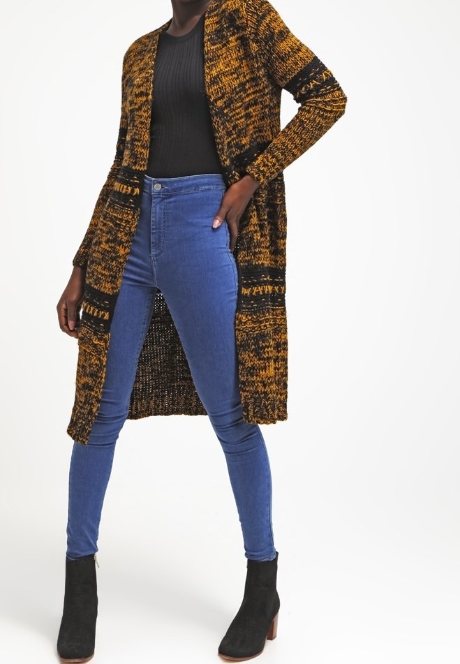 Lång stickad cardigan i svart och senapsgul med öppen front, två fickor och varierande texturer; matchad med blå skinny jeans och ankelboots.