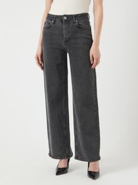 Vaqueros de denim negros de talle alto con un corte holgado, bolsillos, textura deslavada y costuras visibles, combinados con unos tacones negros de punta.