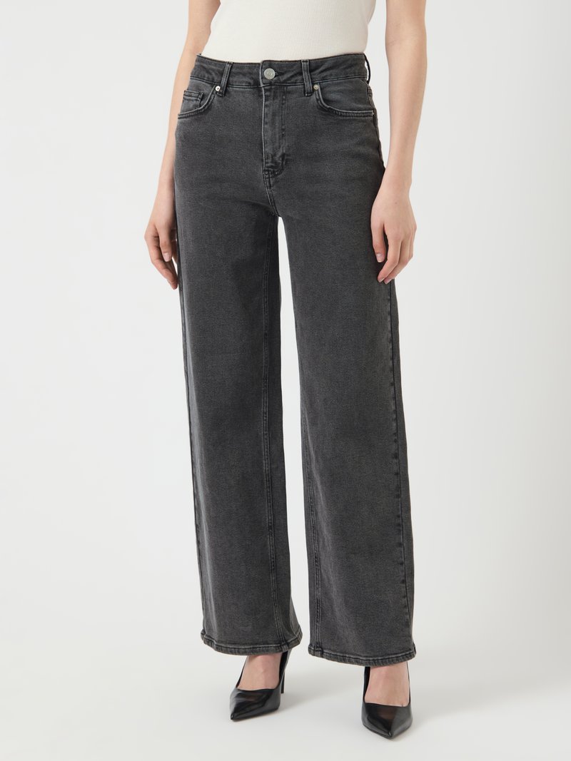 Vaqueros de denim negros de talle alto con un corte holgado, bolsillos, textura deslavada y costuras visibles, combinados con unos tacones negros de punta.