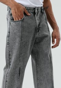 Grijze spijkerbroek met een ontspannen pasvorm, voorzien van een hoge taille, twee steekzakken aan de zijkant en contrasterende stiksels langs de naden.