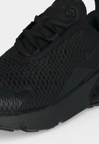 Must Nike toss õhuke ülemise osaga, mustade paelte ja nähtava õhupolstriga tallas, näidates kinga külge ja esiosa.