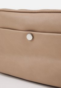 Beżowa skórzana kopertówka o gładkiej fakturze, z zamknięciem na zamek błyskawiczny i srebrnym zatrzaskiem na przedniej kieszeni.