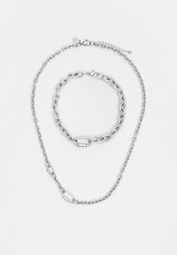 Stříbrná kovová šperková sada obsahující dlouhý náhrdelník a kratší náramek, s propletenými články a hladkým povrchem.