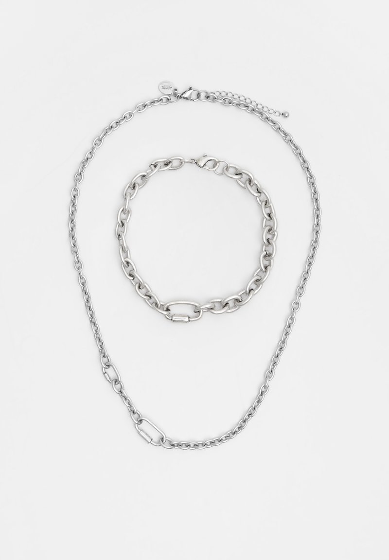 Stříbrná kovová šperková sada obsahující dlouhý náhrdelník a kratší náramek, s propletenými články a hladkým povrchem.