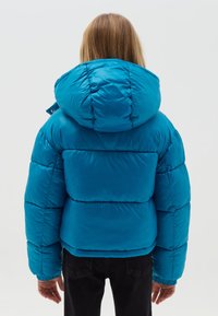 Giacca puffer turchese con grande cappuccio, design trapuntato e polsini elasticizzati. Texture liscia con segmenti imbottiti e cuciture posteriori.