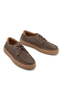 Braune Wildlederschuhe mit runder Zehenpartie, Gummisohle und braunen Schnürsenkeln. Das Obermaterial verfügt über Ziernähte und seitliche Belüftungslöcher.