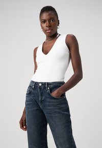 Bodysuit blanc sans manches avec un décolleté en V, associé à un jean taille haute bleu foncé, présentant un style classique à cinq poches.