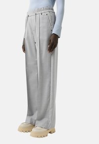 Pantalon large gris clair avec une taille élastique et un cordon de serrage. Le tissu semble texturé, complété par des chaussures à plateforme beiges et épaisses.