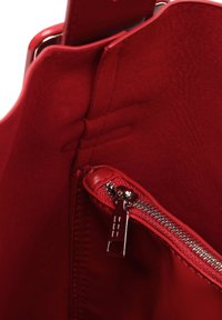 Interiér červené kožené kabelky s kapsou na zip, obsahující metalický zip, hladkou texturu a elegantní design.