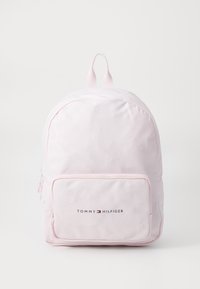 Ljusrosa ryggsäck av slät material med en framficka med dragkedja och "TOMMY HILFIGER"-logotypen i svart. Två justerbara remmar på toppen.