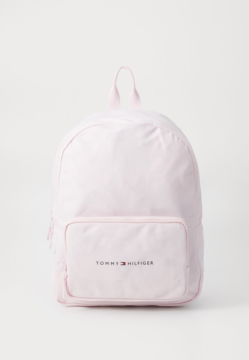 Ljusrosa ryggsäck av slät material med en framficka med dragkedja och "TOMMY HILFIGER"-logotypen i svart. Två justerbara remmar på toppen.