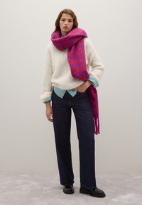 White knit sweater, turquoise striped shirt underneath, dark jeans, and a vibrant pink and purple striped scarf, black chunky boots.