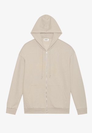 Sweat-shirt à zip beige avec une capuche, des poches avant et des cordons de serrage. Fabriqué en tissu doux avec une texture lisse et des bords côtelés.